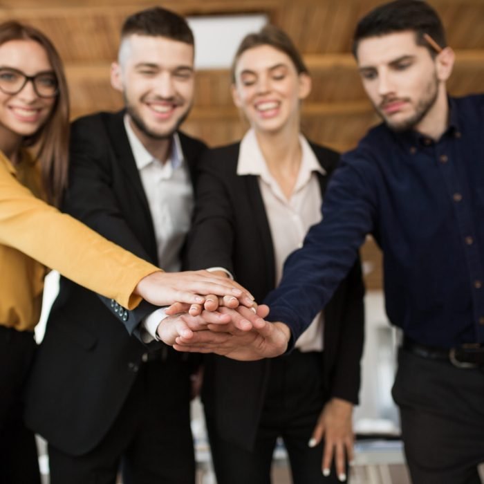 Group of smiling business partners in suits showing unity with their hands together spending time in modern office