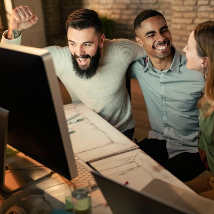 Young start-up team celebrating business success while using computer in the office.